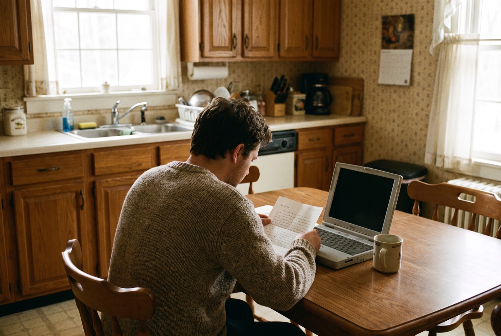 A homeowner at a kitchen table reading a letter beside a laptop